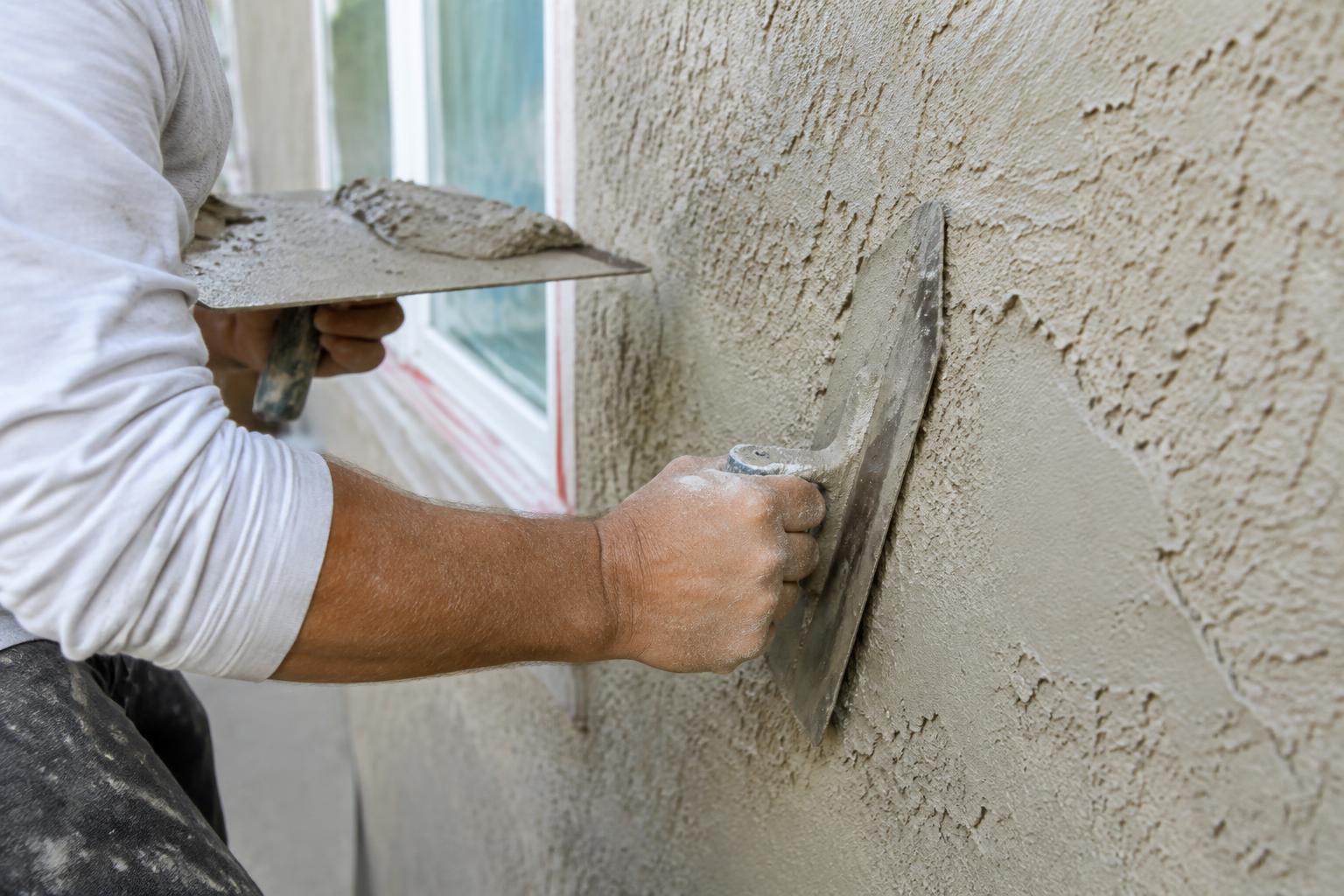 Stucco contractor hand-finishing a textured stucco wall with a steel trowel